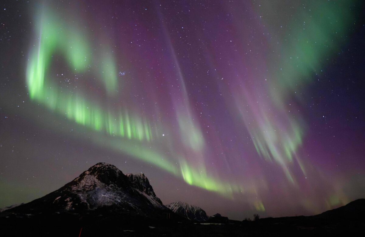 Aurora boreal verde e roxa sob um pico de uma montanha