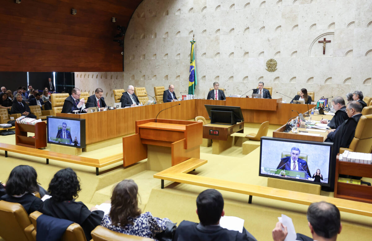 Imagem aberta de plenário do tribunal, com juízes posicionados e um crucifixo ao fundo