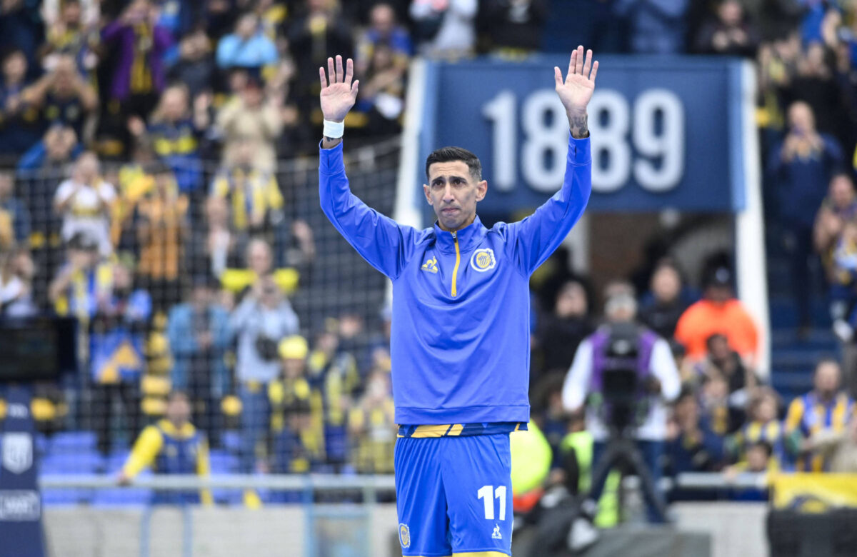 Um jogador de futebol está em campo, vestindo um agasalho azul com detalhes amarelos e o número 11. Ele está com as mãos levantadas, acenando para a torcida. Ao fundo, há uma multidão de torcedores, com bandeiras e camisas nas cores amarelo e azul. O estádio tem uma grande placa com o número 1889 visível.