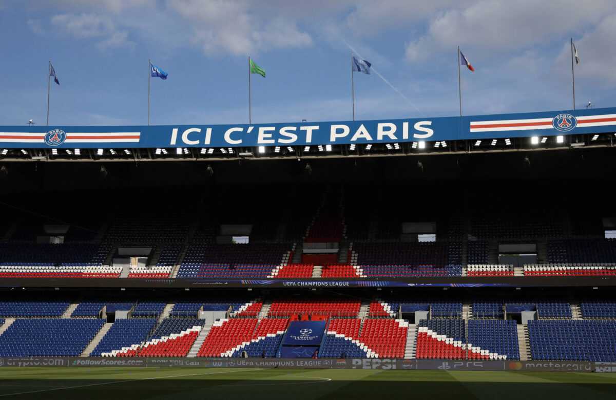 A imagem mostra o interior do estádio do Paris Saint-Germain, com uma grande faixa azul na parte superior que diz