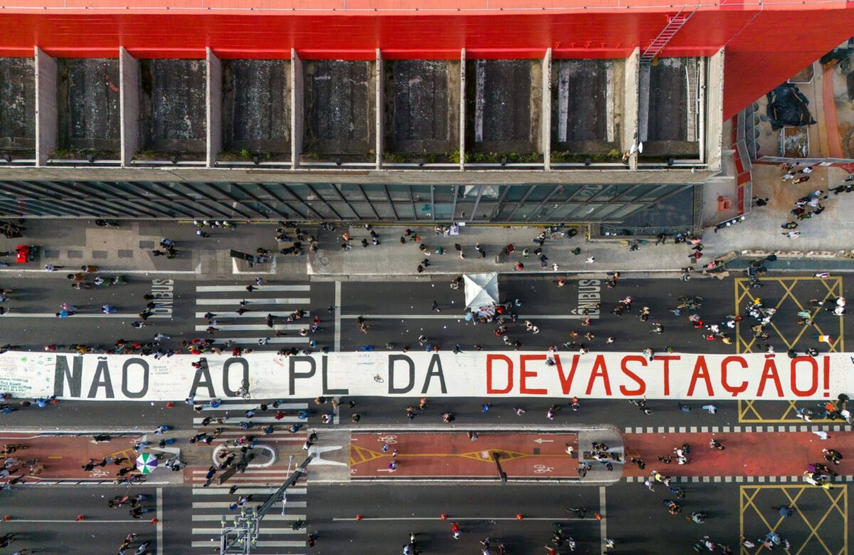 A imagem mostra uma grande faixa estendida em uma rua, com o texto